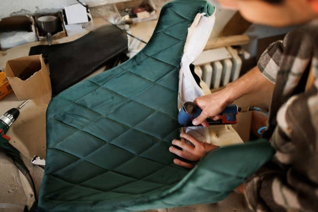 Stock photograph of a young person working as an upholsterer, attaching cloth to a chair with a pneumatic stapler in the workshop